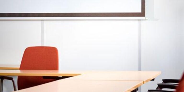 Empty conference room with tables, chairs, and a projector screen.