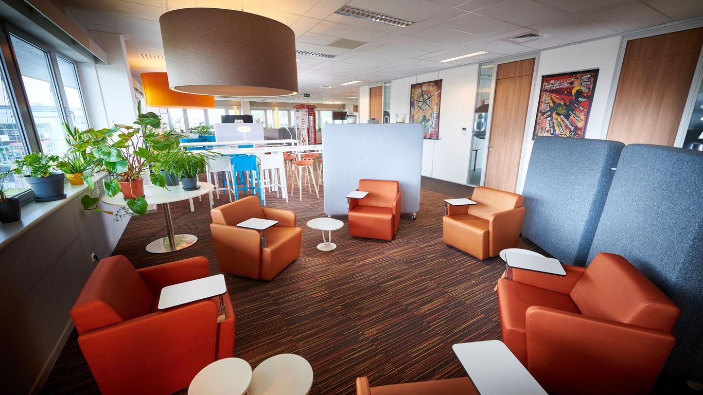 Modern office space with orange chairs, plants, and artwork.