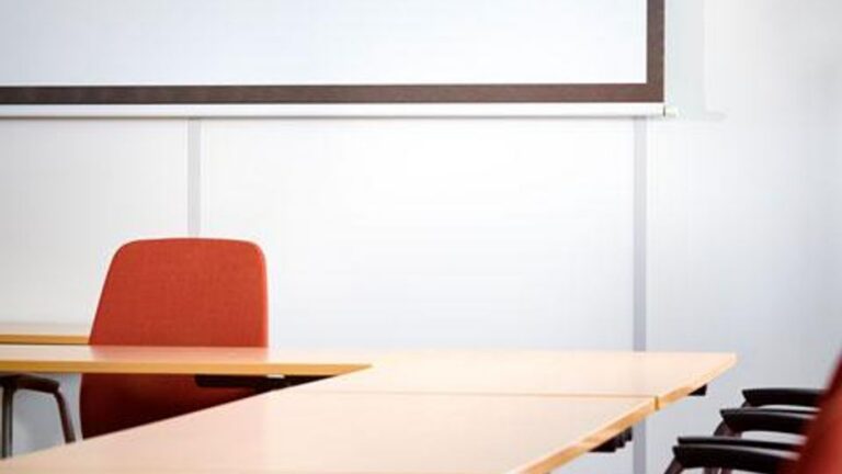 Empty conference room with tables, chairs, and a projector screen.