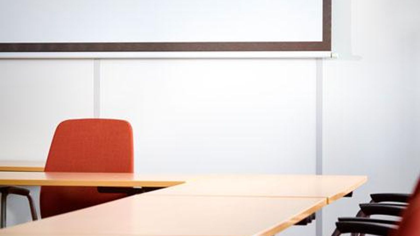 Empty conference room with tables, chairs, and a projector screen.